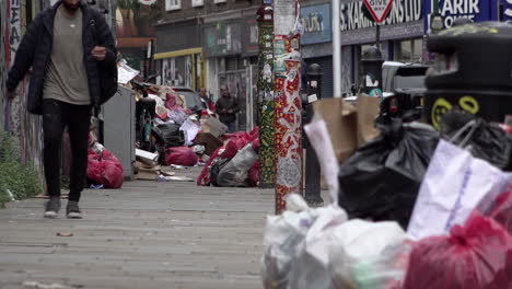 Ein-Mann-Geht-An-Schwarzen-Müllsäcken-Und-Müll-Vorbei,-Die-Sich-Nach-Zweiwöchigen-Müllstreiks-Im-Stadtteil-Tower-Hamlets-Auf-Der-Backsteinstraße-Aufgetürmt-Haben