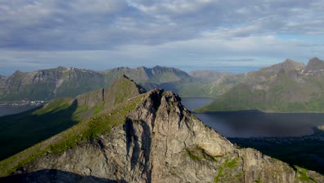 Aerial-forwarding-shot-with-tourists-on-the-mountain-peak-Hesten-enjoying-the-view,-Senja-Island