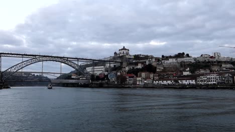 Navigation-on-Douro-River-in-Porto-with-views-of-Luis-I-Bridge,-Portugal,-day