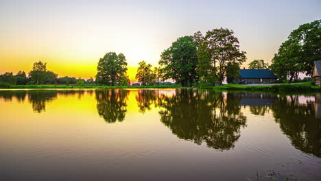 Ein-Orangefarbener-Sonnenuntergang-über-Einem-Spiegelglatten-See-Mit-Einem-Haus-Am-Ufer