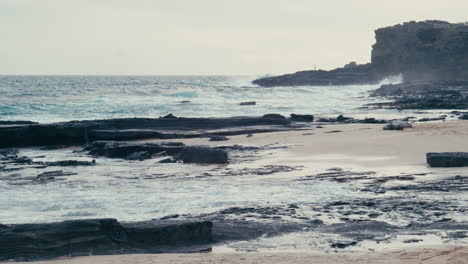 Sandy-Beach-cliffside-landscape-with-waves-splashing-on-volcanic-rocks