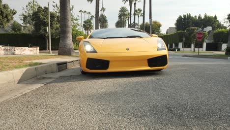 Yellow-Lamborghini-Luxury-Sports-Car,-Pulling-up-and-Stopping-in-Beverly-Hills-Street-Lined-with-Palm-Trees,-Hollywood-California