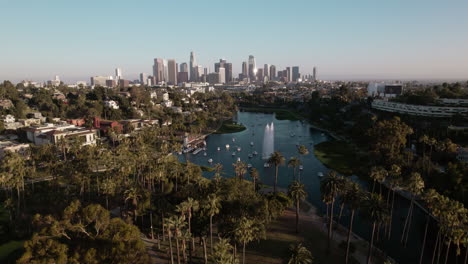 Eine-Drohnenaufnahme-Des-Echo-Park-Lake-Mit-Der-Innenstadt-Von-Los-Angeles-Im-Hintergrund-Zur-Goldenen-Stunde,-Die-In-Die-Innenstadt-Vordringt
