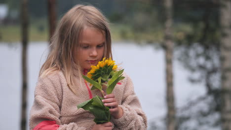 Handheld-slow-motion-shot-of-a-blonde-girl-holding-a-sunflower-found-in-the-finnish-countryside