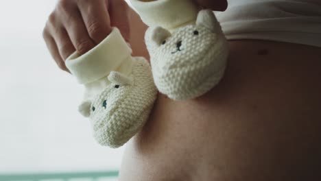 Close-of-video-of-baby-shoes-on-pregnant-abdomen