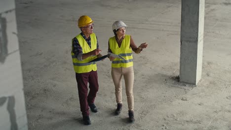 High-angle-view--video-of-male-and-female-caucasian-engineers-discussing-and-pointing-on-the-construction-site.-S