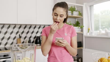 Mujer-Joven-Usando-Teléfono-Móvil-Y-Preparando-El-Desayuno-En-La-Cocina