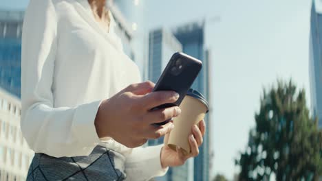 Close-up-video-of-businesswoman-walking-with-phone-and-coffee
