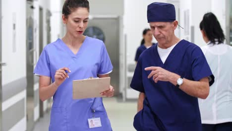 Doctors-discussing-medical-records-and-walking-through-corridor-in-hospital