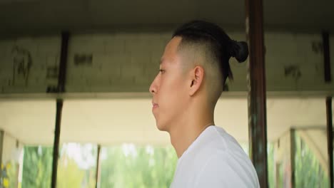 Side-view-of-young-Chinese-man-walking-inside-an-abandoned-building