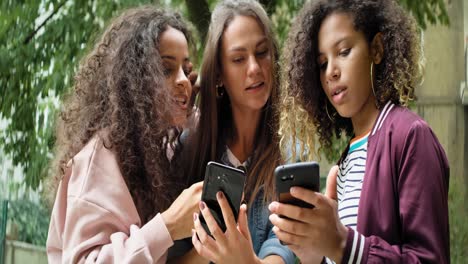 Three-young-friends-using-mobile-phone-outdoors