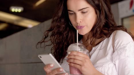 Young-woman-using-phone-and-drinking-smoothie