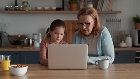 Caucasian-grandmother-and-granddaughter-using-laptop-in-the-kitchen