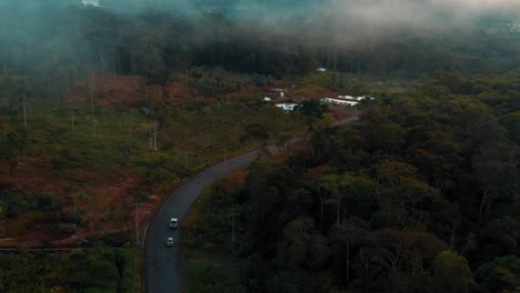 Aerial-View-of-Cars-Driving-Along-Road-Through-Misty-Cloudy-Wild-Jungle-in-Ecuador