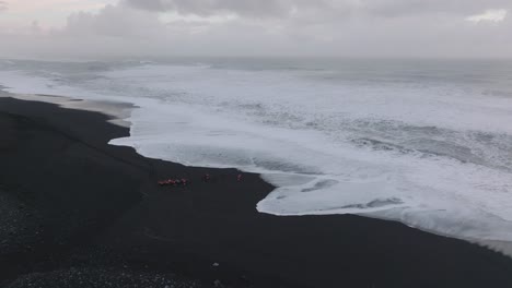 Aerial-view-of-bright-red-quad-bikes-on-Iceland-Sólheimasandur-beach-black-sand,-next-to-the-ocean-waves