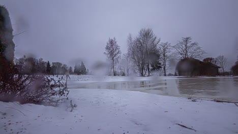 Timelapse-Winter-Background-with-Raindrops-Over-Lens-Across-a-Frozen-Lake-and-Barn-in-the-Countryside-of-Latvia