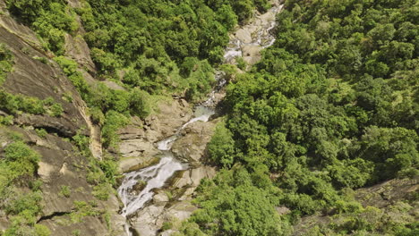 Ella-Sri-Lanka-Aerial-v39-vertical-birds-eye-view-drone-flyover-Ravana-waterfall-capturing-water-flowing-downstream-surrounded-by-cliffside-jungle-lush-greenery---Shot-with-Mavic-3-Cine---April-2023