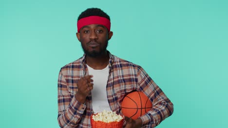 Bearded-african-american-young-man-basketball-fan-holding-ball-doing-winner-gesture,-dancing-alone