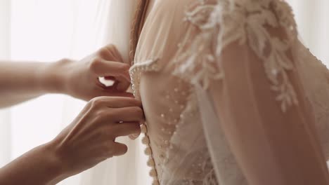 Bridesmaid-ties-and-helps-put-on-wedding-dress,-morning-preparation-of-the-bride-with-white-gown