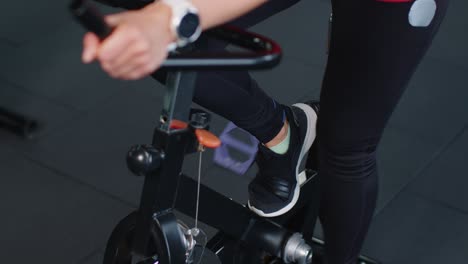 Close-up-athletic-woman-spin-exercising-workout-on-stationary-cycle-machine-bike,-indoors