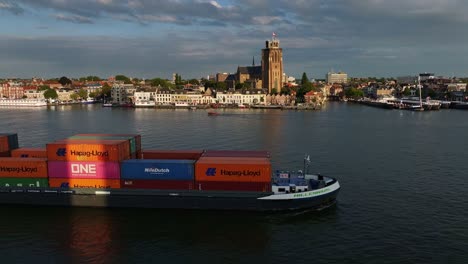 Como-Telón-De-Fondo-De-Dordrecht,-Un-Barco-Portacontenedores-Lleno-De-Mercancías-Navega-Por-El-Río-Oude-Maas.