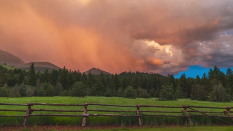 Yellow-orange-vibrant-storm-clouds-move-across-sky-above-grassy-meadow,-time-lapse