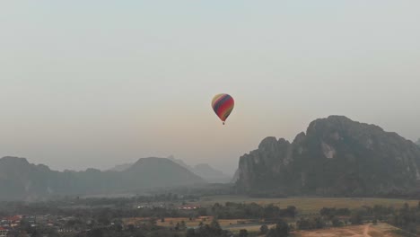 Hot-air-balloon-above-rural-Vang-vieng-Laos-during-sunrise,-aerial
