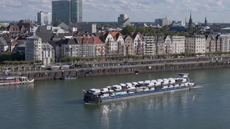 Riverfront-of-Dusseldorf-city-and-cargo-ship-loaded-with-cars,-transportation-on-the-river