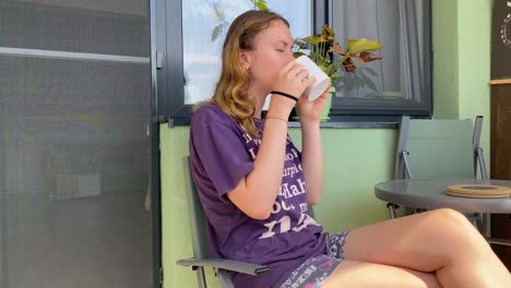 Woman-drinking-from-cup-while-sitting-outside-her-home,-static