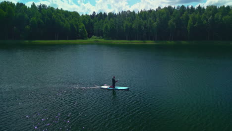 Drone-Orbit-Of-Paddleboarder-on-Lake-Amongst-Green-Trees