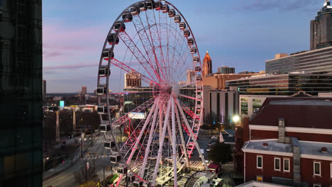 Drone-approaching-shot-of-spinning-Ferris-Wheel-during-sunrise-in-the-morning-in-Atlanta-City,-USA