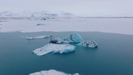 Aerial-view-over-icebergs-in-the-glacial-water-of-Jokulsarlón-lake,-in-Iceland,-during-winter