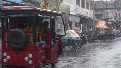 Ländliche-Indische-Stadt-Bei-Regen,-Einheimische-Reisen-In-Elektronischen-Rikschas-Und-Tuk-Tuks-Mit-Blick-Auf-Haushaltswarengeschäfte-Im-Hintergrund