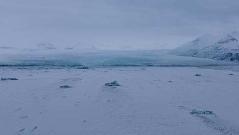 Aerial-panoramic-view-of-the-frozen-Jokulsarlón-lake-area,-with-icebergs-covered-in-snow,-in-Iceland,-at-dusk