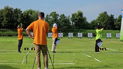 Man-Filming-Behind-Archers-Aiming-To-Targets-In-An-Outdoor-Archery-Range
