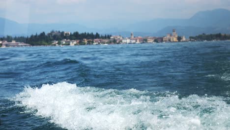Wake-and-white-wash-from-rear-view-of-boat-at-Lake-Garda-Italy,-view-of-european-coastline-behind