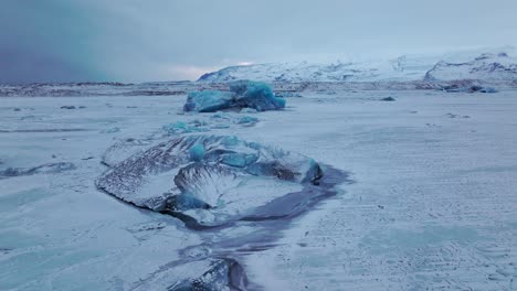 Aerial-panoramic-view-over-icebergs-on-the-frozen-Jokulsarlón-lake-surface,-in-Iceland,-at-dusk