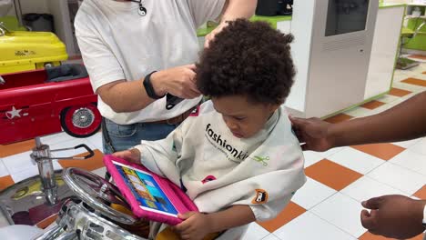 Three-year-old-exotic-black-kid-getting-a-haircut-at-a-children’s-salon-while-his-mother-comforts-him