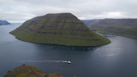 Fishing-boat-drives-past-salmon-farm-rings-offshore-of-Kunoy,-Faroe-Islands