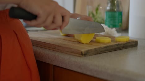 Close-up-of-a-woman-slicing-potatoes-with-a-chef-knife-in-a-small-kitchen-with-natural-light