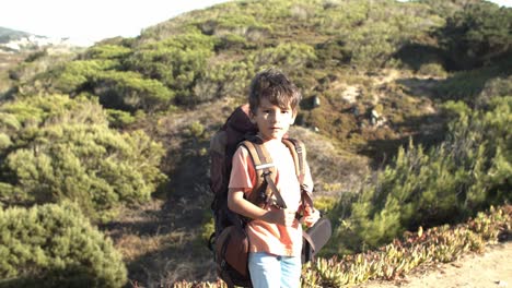 Cute-boy-walking-on-mountain-path,-carrying-big-backpack