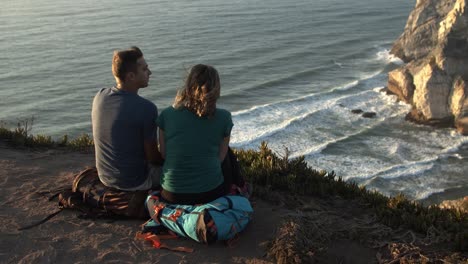 Couple-of-backpackers-taking-break,-sitting-at-cliff