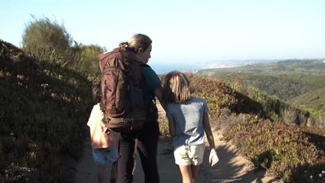 Kids-and-mom-wearing-backpack,-walking-on-path-in-mountains