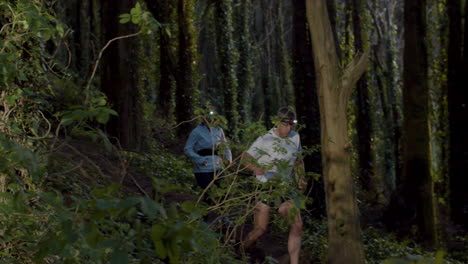 Focused-man-and-woman-with-headlights-running-in-forest-at-dusk