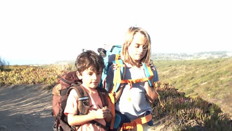 Active-kids-walking-on-mountain-path,-carrying-heavy-backpacks