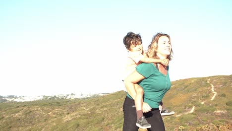 Active-mom-piggybacking-son-kid,-walking-on-mountain-path