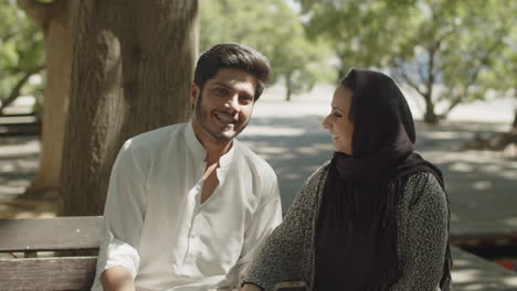 Lovely-muslim-couple-sitting-on-bench-in-park-on-hot-summer-day.