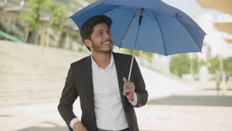 Young-muslim-man-opening-blue-umbrella,-hiding-from-sun.
