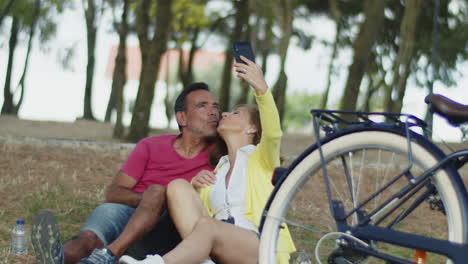 Älteres-Paar-Sitzt-Auf-Gras-Im-Park-Und-Macht-Ein-Selfie