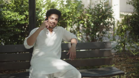 Young-muslim-man-sitting-on-bench,-talking-on-his-cellphone.
